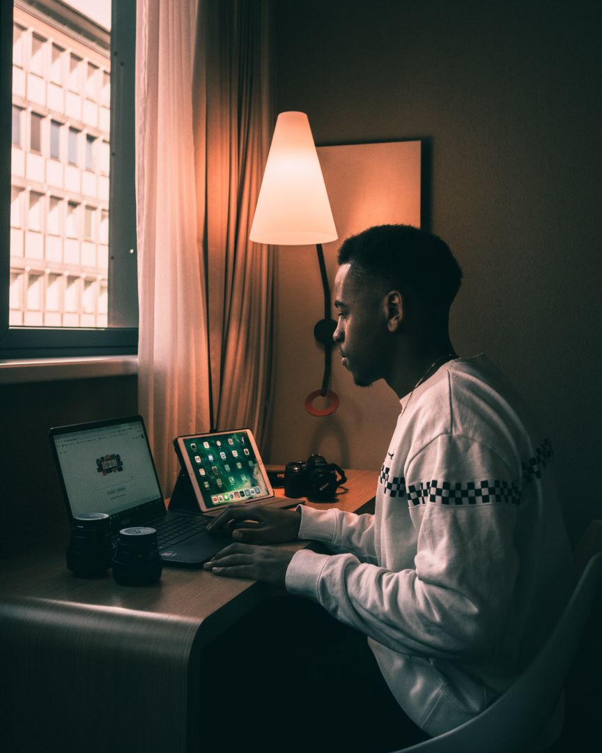A young Black man sitting at a desk in front of a computer and tablet.