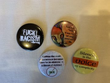 Four buttons Brittyn picked up at the INAPS conference in San Diego. One reads in black and white, "Fuck Racism." Another has a cat and says, "Fuck your 'help,' it was my cat who saved my life. Anther reads, "Calling the cops on a person because they're in distress = a threat of violence," and it has 911 crossed out. The last one reads, "Silence is the voice of complicity."