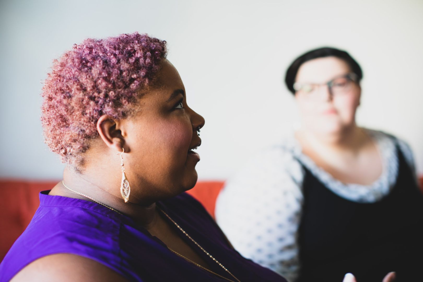 A Black woman with pink hari and a white woman with brown hair sit in a meeting