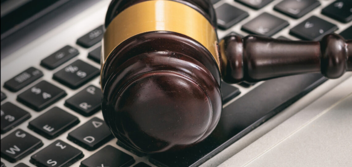 A close-up image of a classic wooden gavel with a gold accent around the hammer head sits on top of a laptop keyboard.
